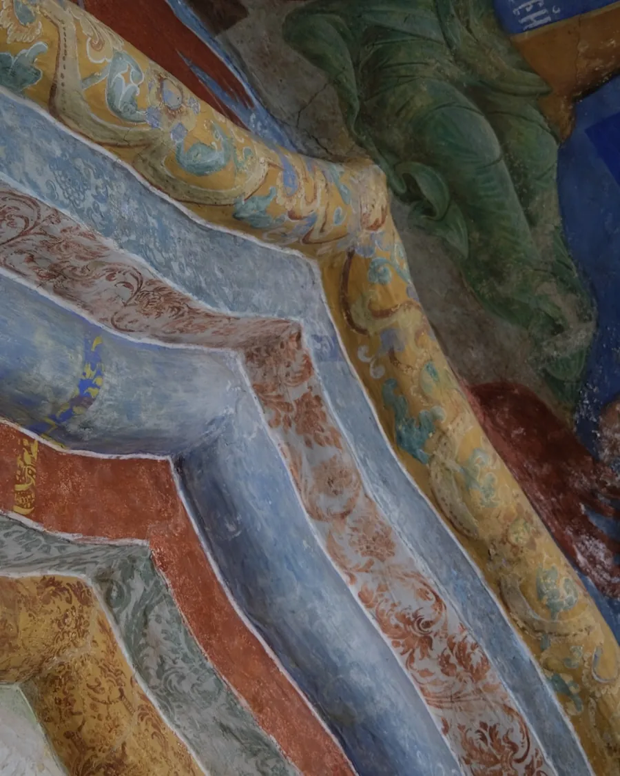 Detalle de una pintura al fresco con pliegues de ropaje en ocres, azules y rojos sobre un enlucido agrietado